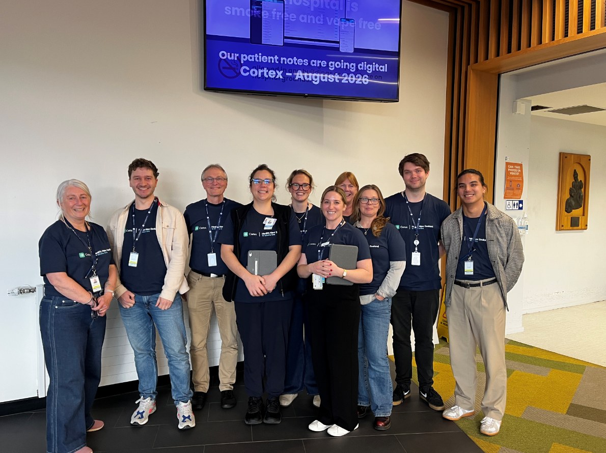 Ten members of the Cortex rollout team standing together in a Timaru Hospital foyer, below a screen reading 'Our patient notes are going digital. Cortex, August 2026'